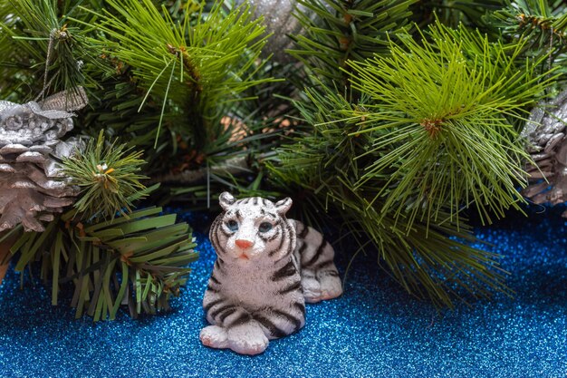 The water tiger is the symbol of the chinese new year 2022. a figurine of a tiger lying on a blue shiny background like on water with fir branches.