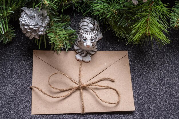 The water tiger is the symbol of the chinese new year 2022. toy tiger holding a craft envelope on a gray shiny background with branches of a spruce. good news concept