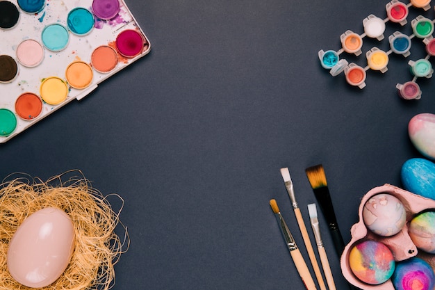 Free photo watercolor paint box and plastic bottle; easter egg; paint brushes on black background