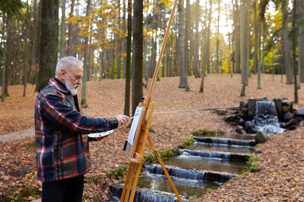 Foto gratuita artista della pittura ad acquerello all'aperto nella foresta con cavalletto e tela