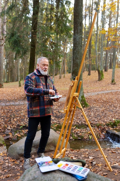 Foto gratuita artista della pittura ad acquerello all'aperto nella foresta con cavalletto e tela