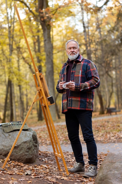 Foto gratuita artista della pittura ad acquerello all'aperto nella foresta con cavalletto e tela