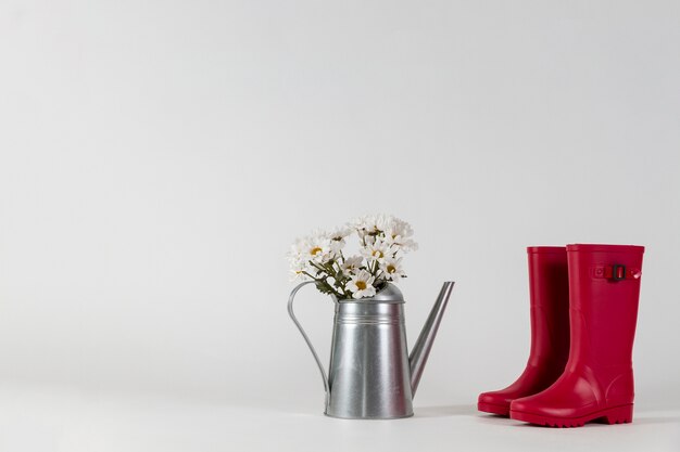 Watering can with flowers next to a pair of red water boots