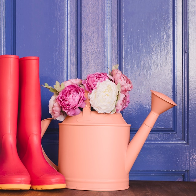 Watering can with roses next to gumboots