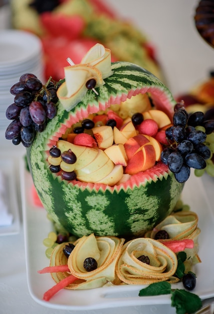 Watermelon full of peaches and grape stands on white plate 