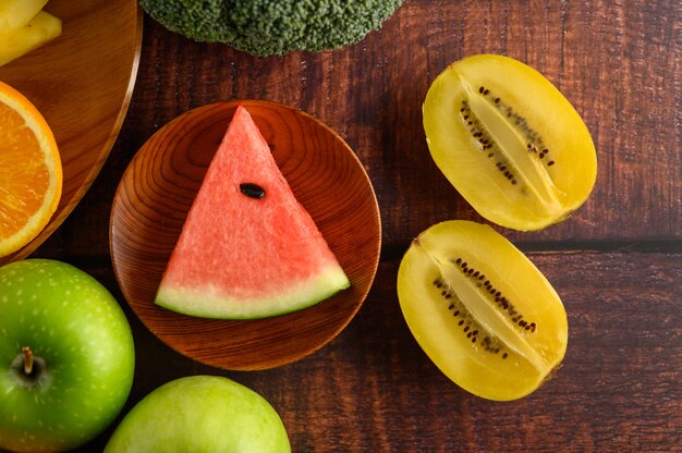 Watermelon, orange, kivi, cut into pieces with apples and Broccoli on a wooden plate.