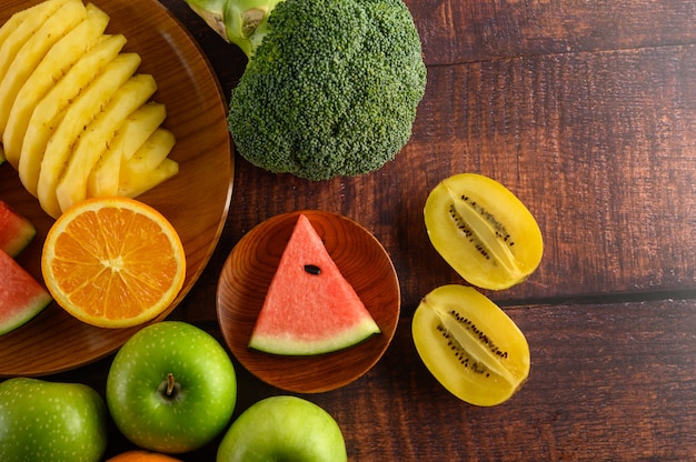 Foto gratuita anguria, arancia, ananas, kiwi tagliati a fette con mele e broccoli su un piatto di legno e un tavolo di legno.