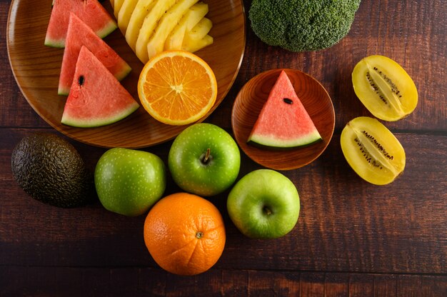 수 박, 오렌지, 파인애플, 키 위 사과와 브로콜리 나무 접시와 나무 테이블에 조각으로 잘라.