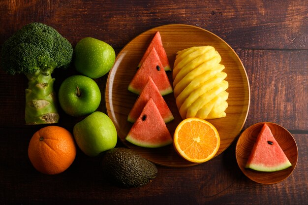 Watermelon, pineapple, oranges, cut into pieces with avocado, Broccoli and apples on wood table. Top view.