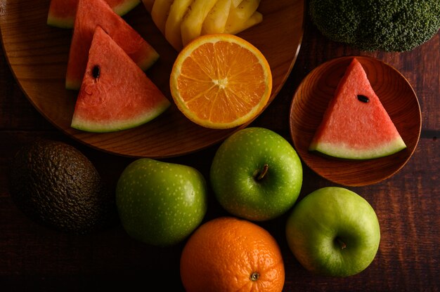 Watermelon, pineapple, oranges, cut into pieces with avocado, Broccoli and apples on wood table. Top view.