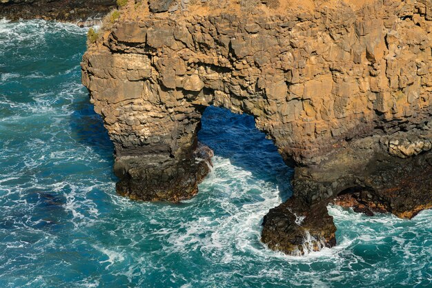 Wave breaking on the rocks in the sea, grotto rock. Oceanic shore rocky formations. Tenerife, Spain