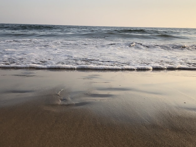 Wavy ocean hitting the sandy beach and gleaming under the colorful sky