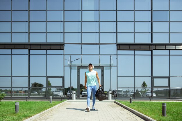 On the way. Sportsman walking down against modern glassed building, airport in megapolis. Before flight to competition