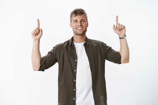 We are champions belong top Portrait of satisfied goodlooking happy blond european male with perfect white smile grinning as pointing up with raised hands showing something awesome and cool