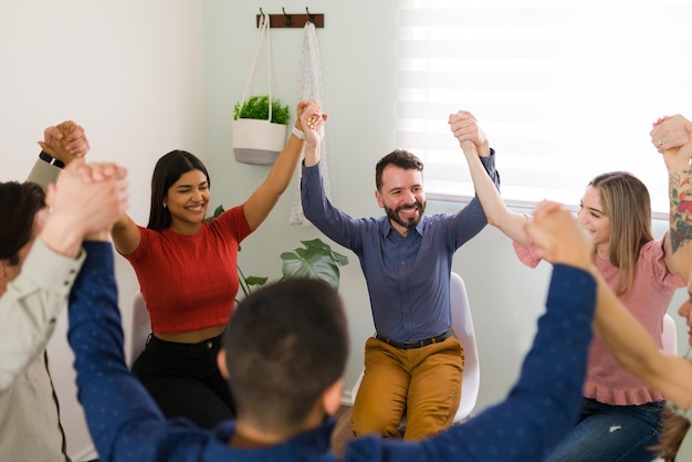 We did it. Excited young women and men holding hands and raising their arms to celebrate the end of their support group to control their addictions