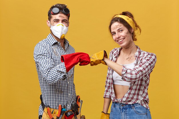 We have done it! Young dirty maintenance workers wearing protective gloves and casual clothes keeping their fists together being glad to finish their work. People, profession, teamwork concept