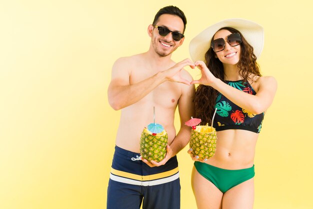 We love each other so much. Romantic couple in love wearing swimsuits making a heart gesture with their hands at the beach