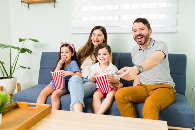 우리는 이 영화를 좋아합니다. 4인 가족이 함께 코미디 영화를 보고 집에서 간식을 먹으며 웃고 있다
