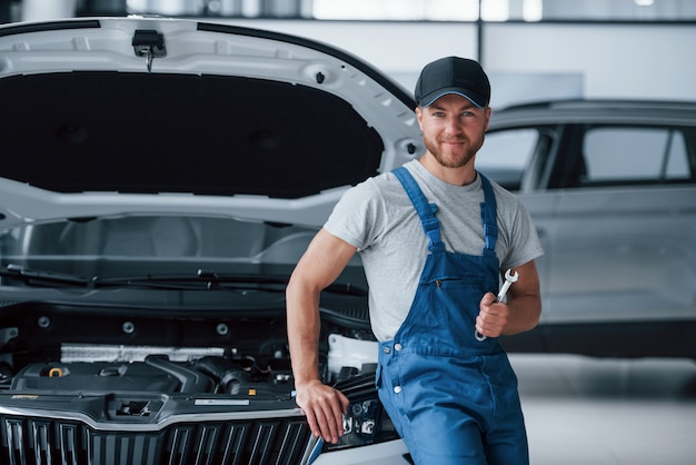 Foto gratuita ripareremo qualsiasi cosa. l'impiegato nell'uniforme di colore blu sta nel salone dell'automobile