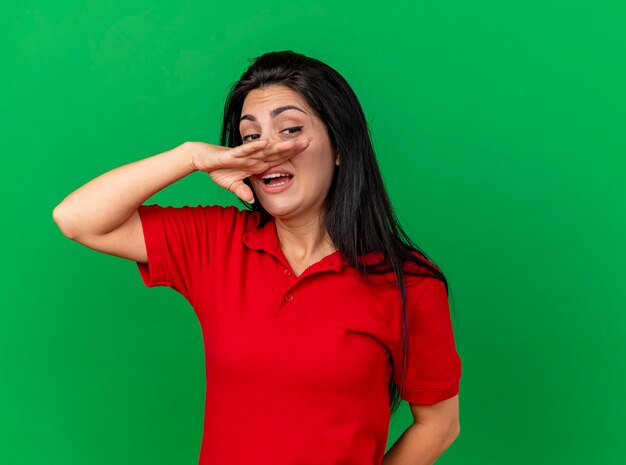 Weak young caucasian ill girl looking at side wiping nose with hand isolated on green background with copy space