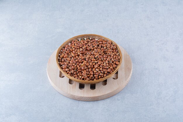 Weaved basket on top of a wooden board, filled with dried red beans on marble background.