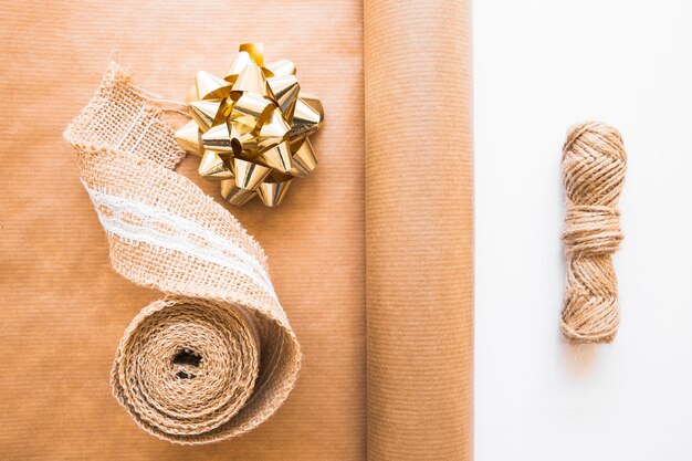 Weaving ribbon; golden bow; brown gift paper and jute string on white background