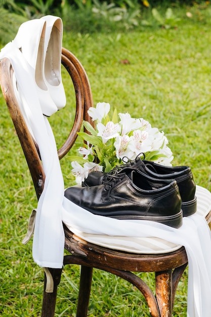 Wedding black shoes and white high heels with flower bouquet on wooden chair in the garden