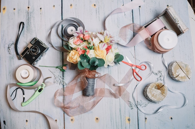 Free photo wedding bouquet lies among ribbons, camera and scissors on the t