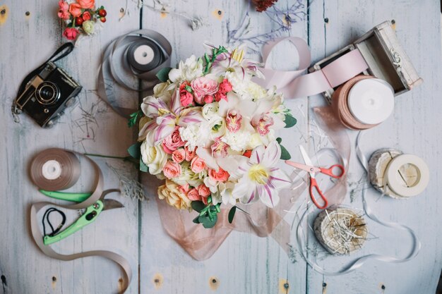 Wedding bouquet lies among ribbons, camera and scissors on the t