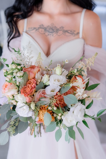 Wedding bouquet made of eustoma and eucalyptus, bridal dress with open decollete and tattoo on the breasts