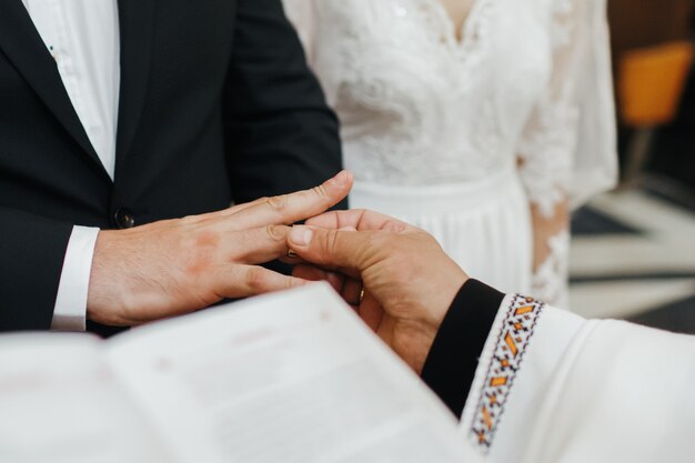 Wedding ceremony. Priest puts wedding ring on groom's hand