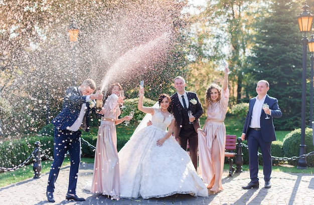 Свадебная пара и лучшие друзья пьют шампанское и празднуют в парке день свадьбы