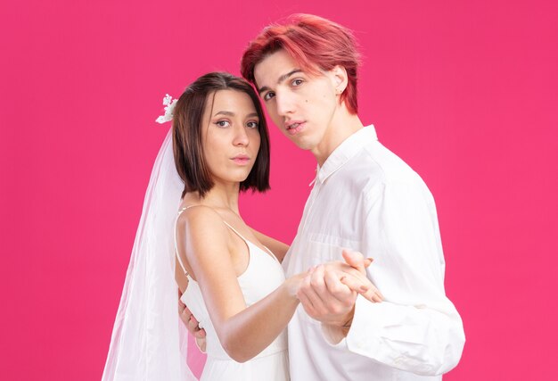 Wedding couple of groom and bride happy in love together dancing smiling posing over pink wall