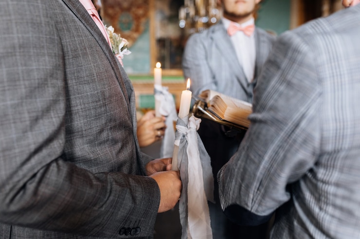 無料Photo 結婚式のカップルは教会の神聖な結婚式で灰色のリボンでキャンドルを保持しています。
