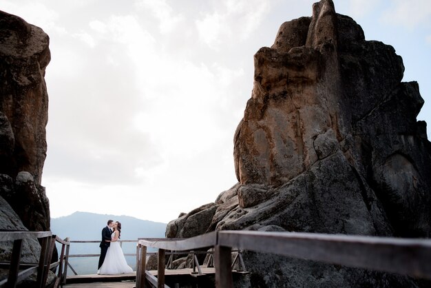 Wedding couple is standing on the wooden bridge between two high cliffs and kissing, wedding adventure