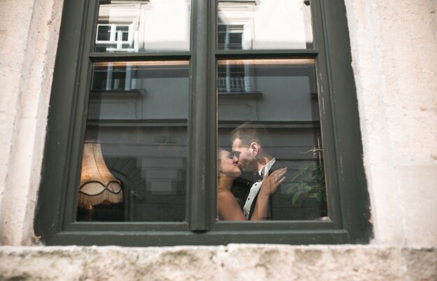 Wedding couple kissing behind window