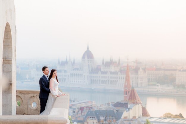 ブダペストの素晴らしい景色を望む古い歴史的建造物の石造りのバルコニーでの結婚式のカップル