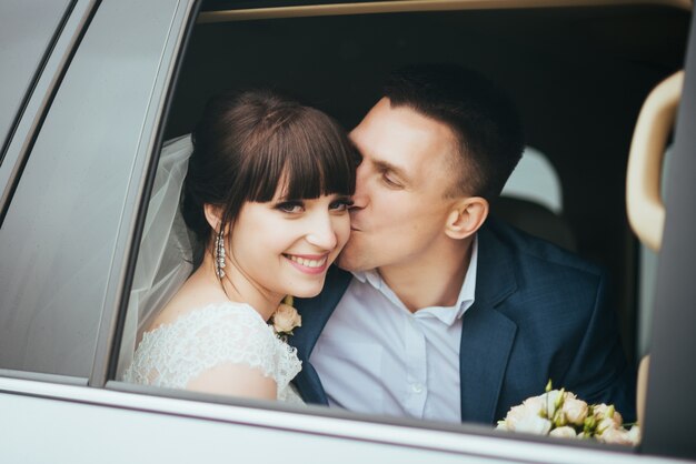 Giorno del matrimonio. il bacio di nozze, lo sposo felice e bello bacia la sposa in automobile di nozze