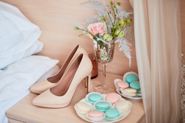 Arredamento di nozze scarpe da sposa beige, bouquet e piatto con amaretti stanno sul tavolo