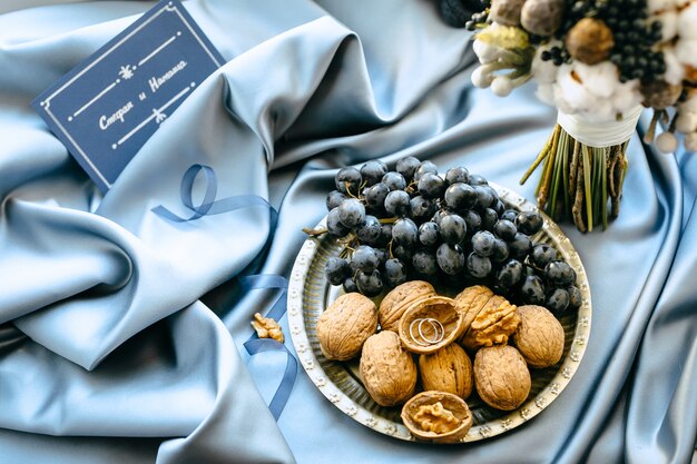 Украшения свадьбы с виноградинами и гайками в плите на голубой предпосылке ткани, взгляде высокого угла.