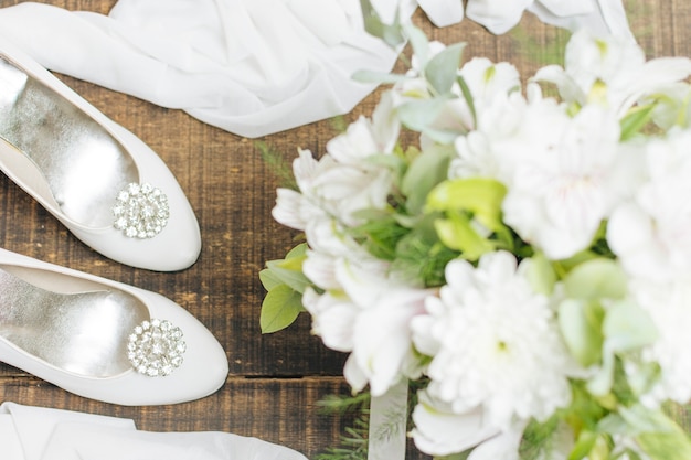 Bouquet di fiori da sposa; tacchi alti e sciarpa sulla sedia di legno