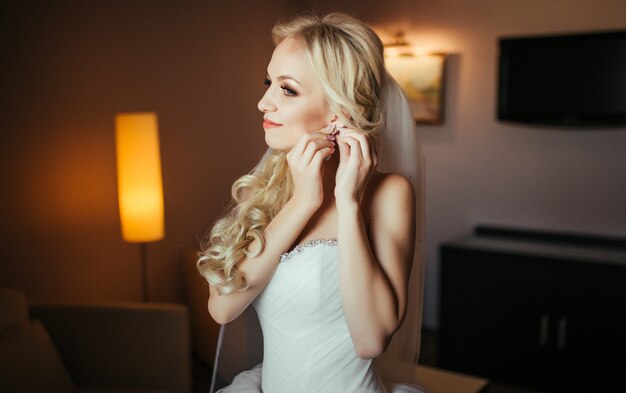 Wedding preparation. Beautiful, happy bride dresses earrings before wedding. 