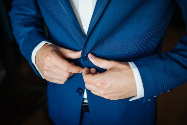 Wedding preparation. Groom buttoning his blue jacket before wedding.