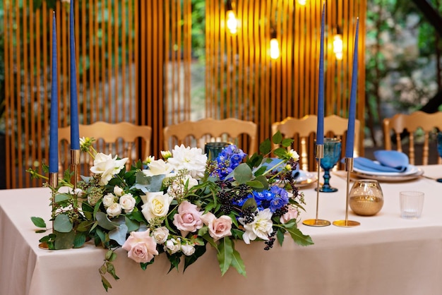 結婚式の幹部会、花、緑、青、金色の新婚夫婦のための宴会テーブル。結婚式のテーブルの緑豊かなフラワーアレンジメント。輝く電球。ソフトセレクティブフォーカス。
