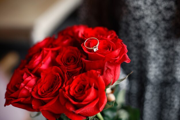 여자의 손가락에 결혼 반지. 빨간 장미 꽃다발입니다. 약혼 선물.