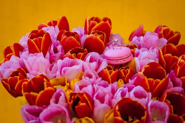 Wedding ring stands on pink macaroon on a bouquet of tulips