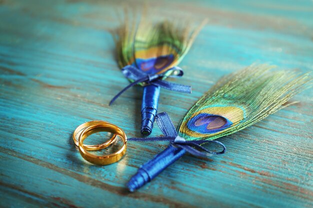 나무 배경에 공작 깃털이 있는 결혼 반지와 부토니에르