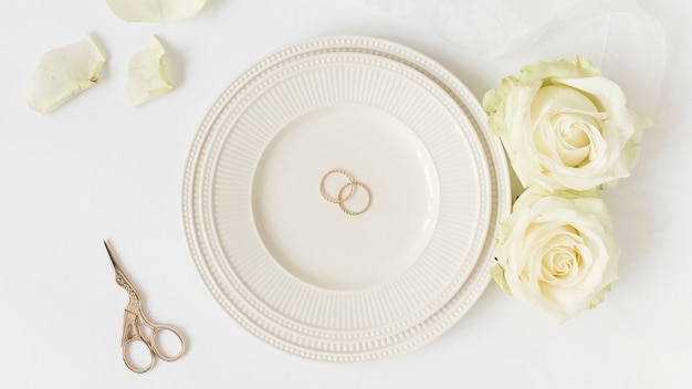 Wedding rings on ceramic plate with roses and scissor on white background