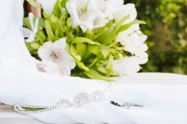 Wedding rings; crown; scarf near the flower bouquet on table