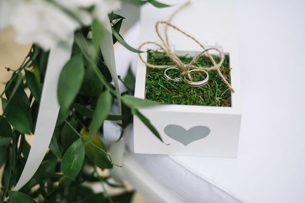 Wedding rings lie on green grass in white box